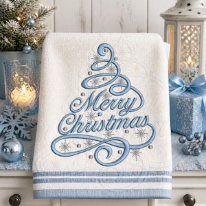 May include: White Christmas-themed towel with a blue embroidered design. The design features a stylized Christmas tree and the words "Merry Christmas" in elegant script. The towel has a blue border.