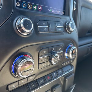 May include: Close-up of a car's dashboard with a digital display showing "81° 11:02". The dashboard has several buttons and knobs, including a temperature control knob with a "68" display and an "AUTO" setting.