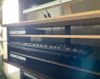 May include: A black computer keyboard sits on a shelf in a wooden entertainment center. The shelf is made of light-colored wood and has a black frame. A computer monitor is visible above the shelf.