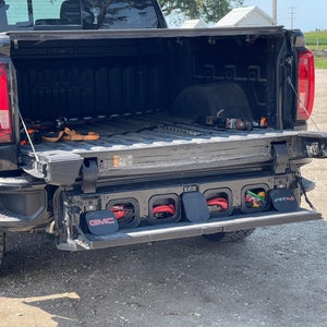 May include: Black pickup truck with the tailgate down, revealing a storage system with multiple compartments. The compartments are labeled with the GMC logo and the text "ATC4".