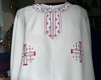May include: White liturgical vestment with red embroidered crosses and geometric patterns. The vestment has a V-neck and long sleeves.