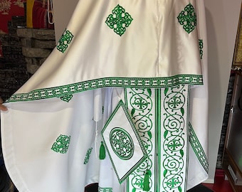May include: White liturgical vestment with green embroidered details. The vestment features a large, flowing cape with a smaller, fitted piece underneath. The embroidery includes intricate floral patterns and crosses.