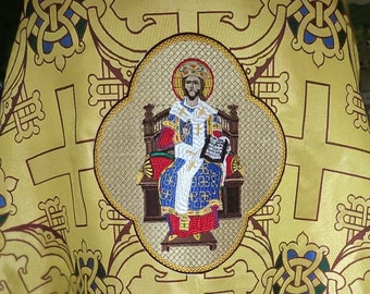 May include: A gold and blue embroidered religious vestment with a central image of Jesus Christ sitting on a throne. The vestment features a repeating pattern of crosses and intricate designs.