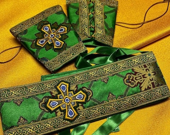 May include: A set of green liturgical vestments with gold trim and embroidered crosses. The vestments include a stole, a pair of cuffs, and a cincture.
