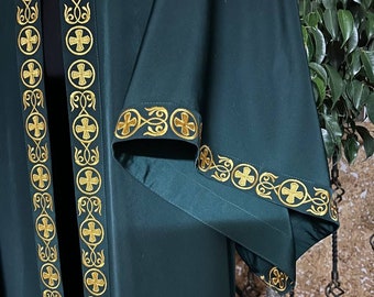 Puede incluir: Una túnica verde oscuro con ribetes bordados en oro que presentan un diseño de cruz. La túnica tiene mangas largas y un diseño largo y fluido.