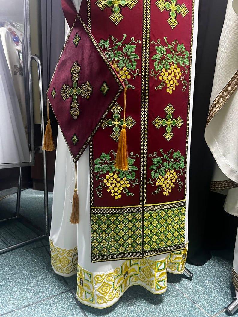 K&ouml;nnte beinhalten: Ein wei&szlig;es liturgisches Gewand mit einem roten und goldenen bestickten Feld mit Trauben und Kreuzen. Das Gewand hat eine passende rote und goldene bestickte Tasche mit einem Kreuz.