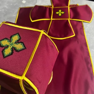 K&ouml;nnte beinhalten: Ein liturgisches Set in Burgunderrot mit goldenen Verzierungen und gestickten gr&uuml;nen und gelben Kreuzen. Das Set beinhaltet ein Kelchtuch und eine Burse.