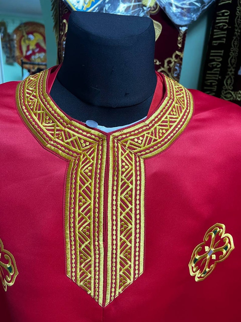 May include: A red liturgical vestment with gold embroidery. The vestment features a detailed gold embroidered collar and a central panel with vertical gold patterns. Decorative gold and green embroidered floral designs are on the lower part of the vestment.