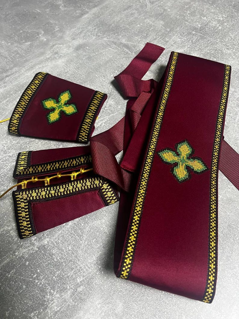 K&ouml;nnte beinhalten: Ein Set aus bordeauxroten Samt-Sch&auml;rpen mit goldenen und schwarzen Verzierungen. Jede Sch&auml;rpe ist mit einem gr&uuml;nen und gelben gestickten Kreuz verziert.