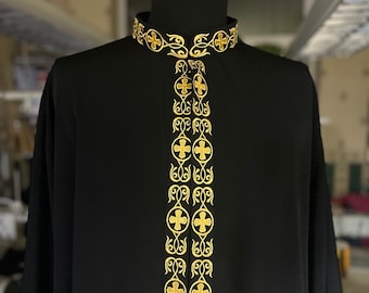 Puede incluir: Una sotana negra con un patrón bordado en oro de cruces y espirales. La sotana tiene un cuello alto con una banda bordada en oro.