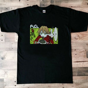 Puede incluir: Camiseta negra con un estampado gráfico de un personaje de anime comiendo fideos. El texto "FLCL" está impreso en la camiseta.