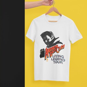 Könnte beinhalten: Weißes T-Shirt mit einem Schwarzweißbild von Andrew Dice Clay. Der Text "Andrew Dice Clay Living Legend Tour" ist in Rot, Gelb und Blau gedruckt.