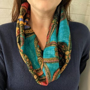 May include: A teal blue infinity scarf with a paisley pattern in gold, red, and black. The scarf has a sparkly finish.