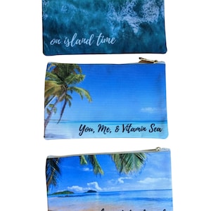 May include: Three zippered pouches with beach-themed designs. The top pouch has a blue and green ocean wave design with the text "on island time". The middle pouch has a blue sky and palm tree design with the text "You, Me, & Vitamin Sea". The bottom pouch has a beach scene with the text "sunshine state of mind".