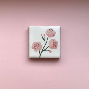 Könnte beinhalten: Eine weiße Keramikfliese mit handgemaltem Design von rosa Kirschblüten auf einem grünen Stiel.