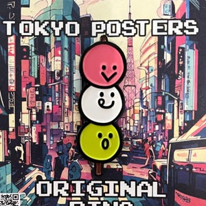 May include: A metal enamel pin featuring three stacked dango spheres in pink, white, and lime green, each with a simple black facial expression. The pin is attached to a square backing card displaying a colorful Tokyo street scene with the text TOKYO POSTERS ORIGINAL PINS and a QR code.
