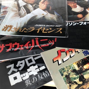 Puede incluir: Una colección de cinco cintas VHS con texto japonés en las portadas. Las cintas son para las películas "The Taking of Pelham One Two Three", "James Bond 007: Licencia para matar", "El Fugitivo", "Rocky IV: La historia de una amistad", y "Conan el Bárbaro".