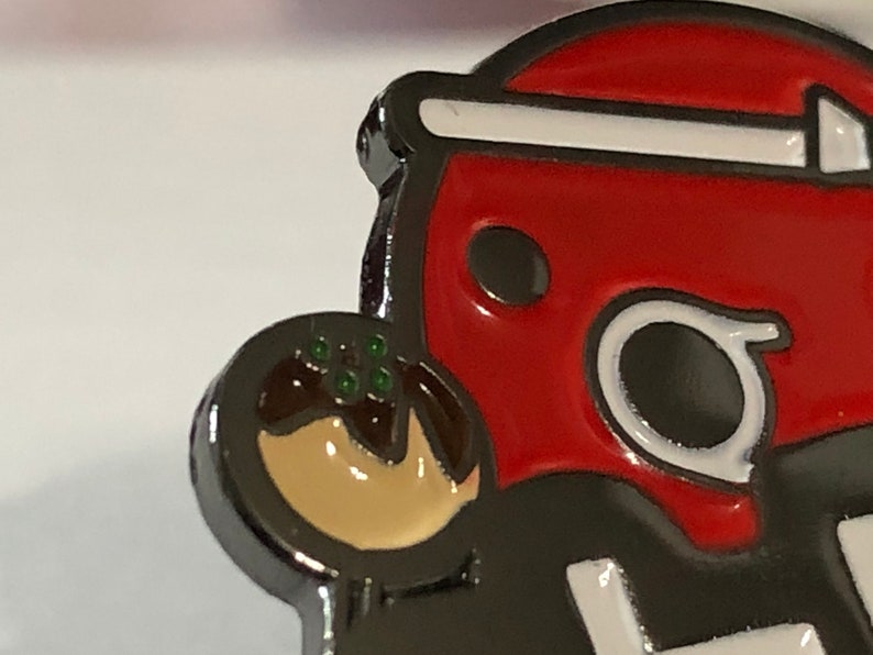 May include: A red and white enamel pin of a cartoon character holding a brown and beige takoyaki. The character has a black eye and a white outline.