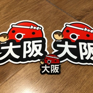 May include: Two red and white stickers with a cartoon octopus holding a takoyaki and the text "大阪" in black. A smaller red and white pin with the same design and text.