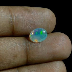 Op de afbeelding: Een witte ovale opaal edelsteen met iriserende groene, blauwe en oranje flitsen.