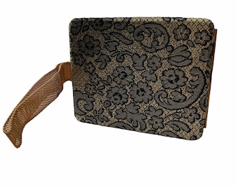 Puede incluir: Un bolso de mano negro y dorado con un estampado floral y una correa marrón.