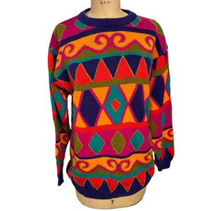 May include: A colorful, geometric patterned sweater in shades of purple, orange, red, green, and yellow. The sweater has a crew neck and long sleeves.