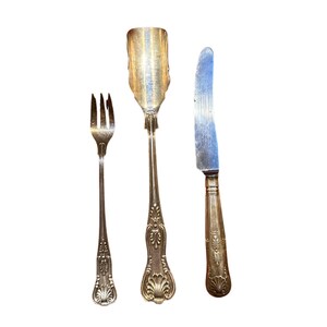 May include: A set of three silver-plated utensils, including a fork, a knife, and a spoon. The utensils have ornate handles with a floral design.