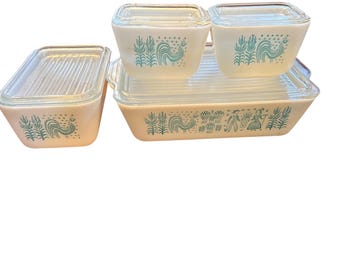 Puede incluir: Un juego de utensilios de cocina Pyrex vintage en crema con diseños de gallos y flores turquesas. El juego incluye una fuente rectangular para hornear, dos recipientes cuadrados y un recipiente rectangular, todos con tapas de vidrio transparente.