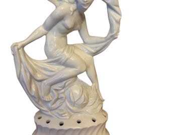 May include: White porcelain figurine of a woman draped in fabric, standing on a round base with holes for flower stems.