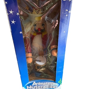 May include: An animated Nutcracker drummer figure in a blue box. The Nutcracker is dressed in a red coat, gold crown, and has a white beard. The box has white stars and the text "Animated Nutcracker Drummer".
