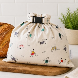 May include: A cream-colored fabric drawstring bag with a black plastic buckle closure. The bag features a repeating pattern of small, stylized cartoon animals in various colors and the printed words take and right. A white tag reads LittleMiddle.