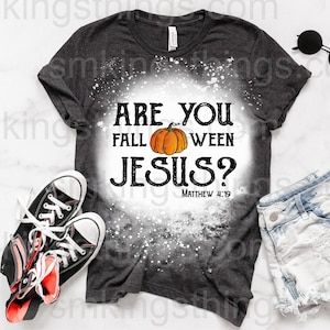 May include: A dark gray t-shirt with a bleach splattered design. The shirt has the text "Are you fall-ween Jesus?" with a pumpkin graphic and the scripture reference "Matthew 4:19".