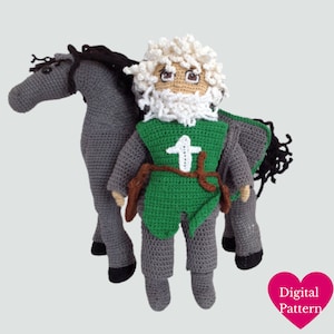 Pode incluir: Padrão de crochê para um cavaleiro e um cavalo. O cavaleiro está vestindo uma túnica verde com uma cruz branca e um cinto marrom. O cavalo é cinza com crina e cauda pretas.