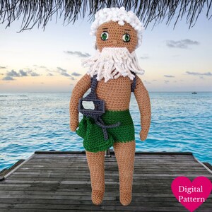 Pode incluir: Boneca de crochê de um velho com barba, cabelo e sobrancelhas brancas, usando calções verdes e uma bolsa cinza. A boneca tem pele castanha e está em um cais de madeira com uma praia e um oceano ao fundo. As palavras "Digital Pattern" estão em um coração rosa.