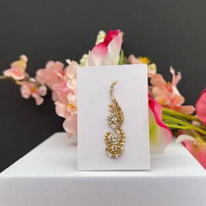 May include: A gold and white rhinestone bindi with a floral design. The bindi is on a white card.