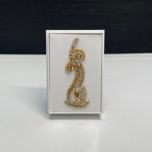 May include: A gold and silver decorative piece with a floral design, displayed in a white box.