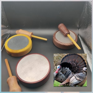 May include: Three wooden turkey call targets with a wooden striker. The targets are made of different woods and have different finishes. The striker is made of a light wood and has a dark brown finish. The targets are used for practicing turkey calls.