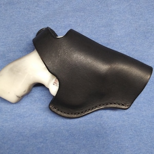 May include: A black leather holster with a stitched border, holding a white handgun. The holster is designed to securely carry the firearm. The image is set against a blue background.