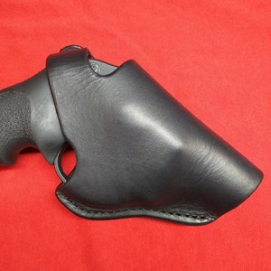 May include: A black leather holster for a handgun. The holster is designed to fit snugly around the gun and has a stitched seam around the edge.