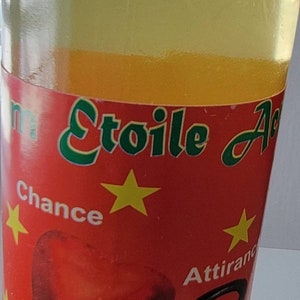 May include: A clear glass bottle with a white cap, filled with a yellow liquid. The bottle has a red label with green text and yellow stars. The label includes the words "Chance", "Attirance", and "Succ&egrave;s".
