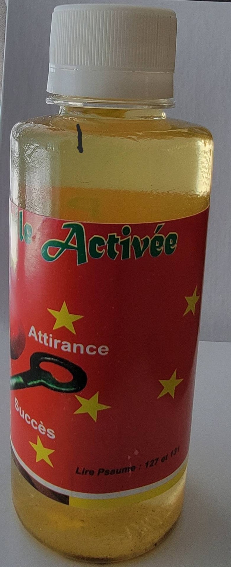 May include: A clear glass bottle with a white cap, containing a yellow liquid. The bottle features a red label with the words "le Activ&eacute;e" in green, yellow stars, and the words "Attirance" and "Succ&egrave;s".