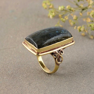 May include: A gold ring with a large, rectangular, dark blue labradorite gemstone set in a gold bezel. The ring has a decorative, ornate band.