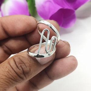 Peut inclure: Une bague en argent avec un design ouvert unique. La bague est composée de deux bandes, l'une étant une bande simple et l'autre une bande avec un design ouvert. La bague est présentée sur un doigt.