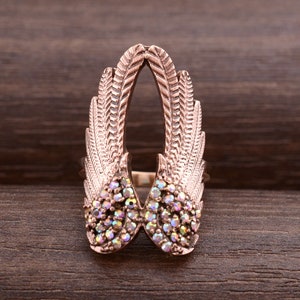 May include: A rose gold ring with a design of two wings with iridescent rhinestones.