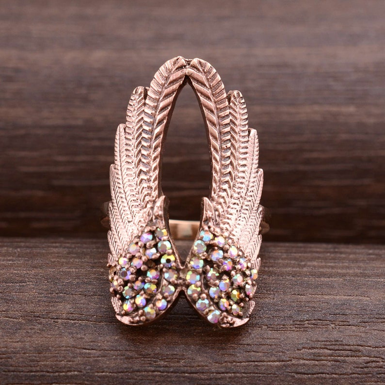 May include: A rose gold ring with a design of two wings with iridescent rhinestones.