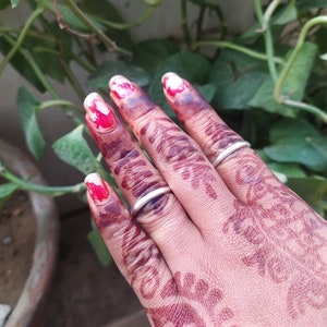 May include: A hand with henna designs on the fingers and palm, wearing two silver rings. The fingernails are painted with red and white nail polish.