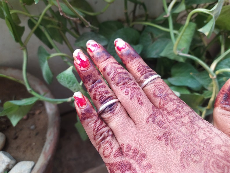 May include: A hand with henna designs on the fingers and palm, wearing two silver rings. The fingernails are painted with red and white nail polish.