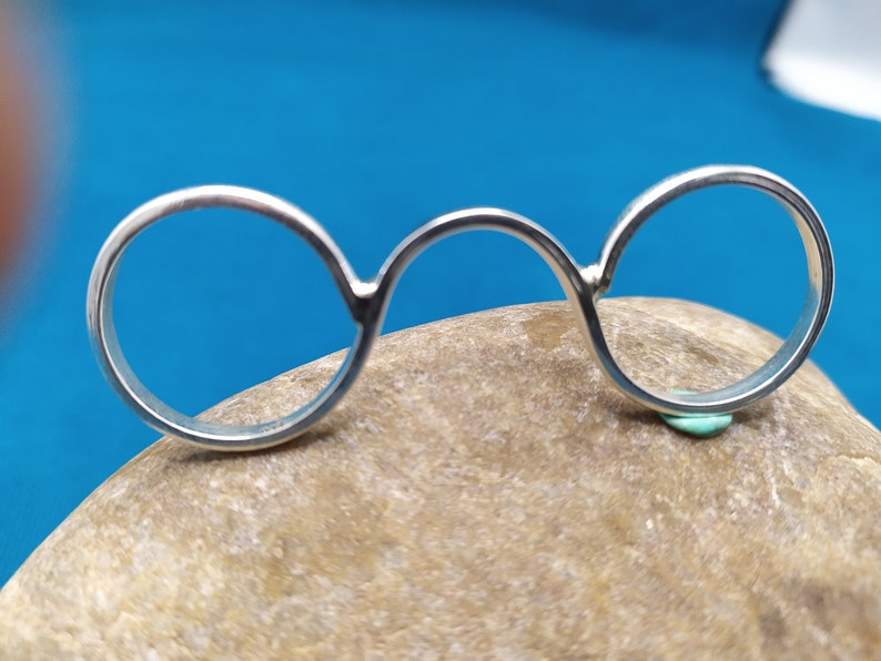 May include: A silver ring with three connected circles. The ring is resting on a brown rock.