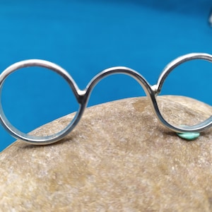 May include: A silver ring with three connected circles. The ring is resting on a brown rock.