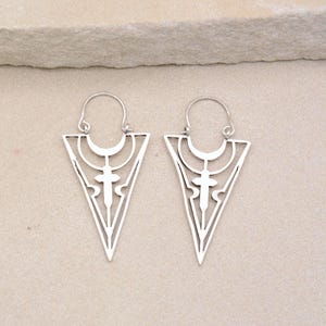 May include: A pair of silver triangle-shaped earrings with a geometric design. The earrings have a hoop closure.